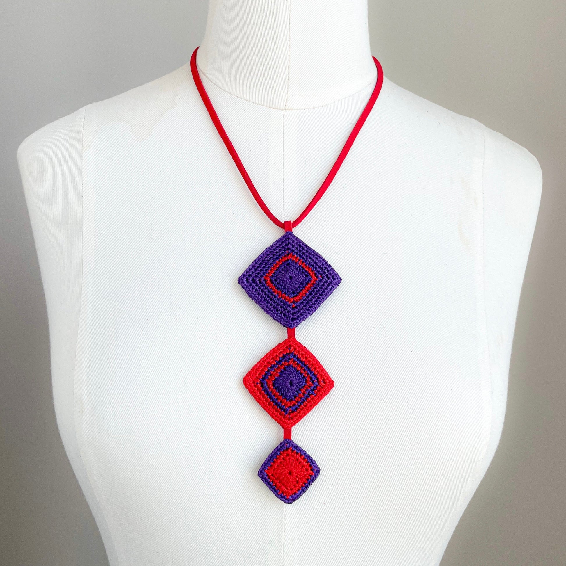 Tessera Necklace with red and purple geometric pendant on a mannequin against a gray background