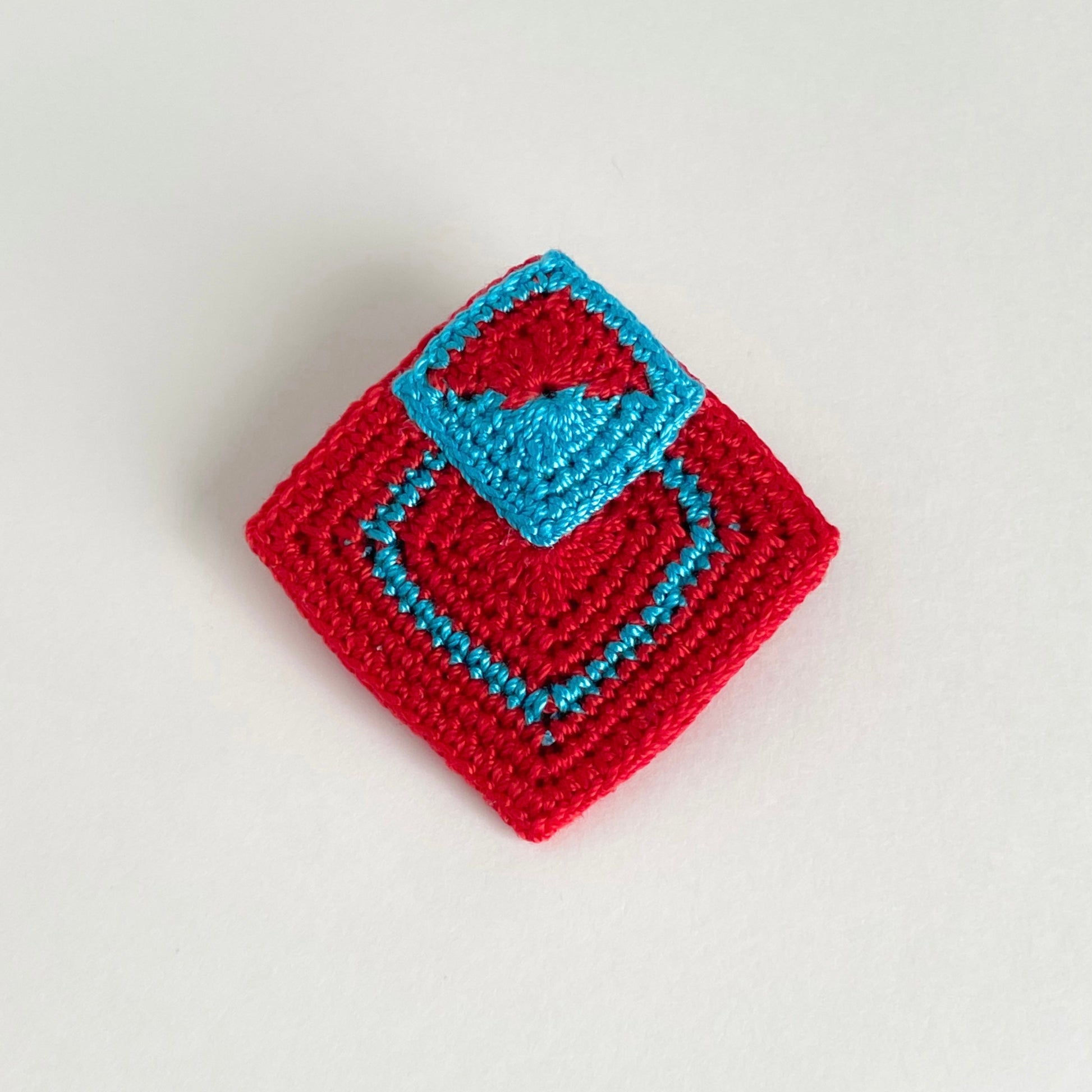 Handmade crochet geometric brooch in red and Caribbean blue (turquoise) with layered square motifs by Crochet by Heart.