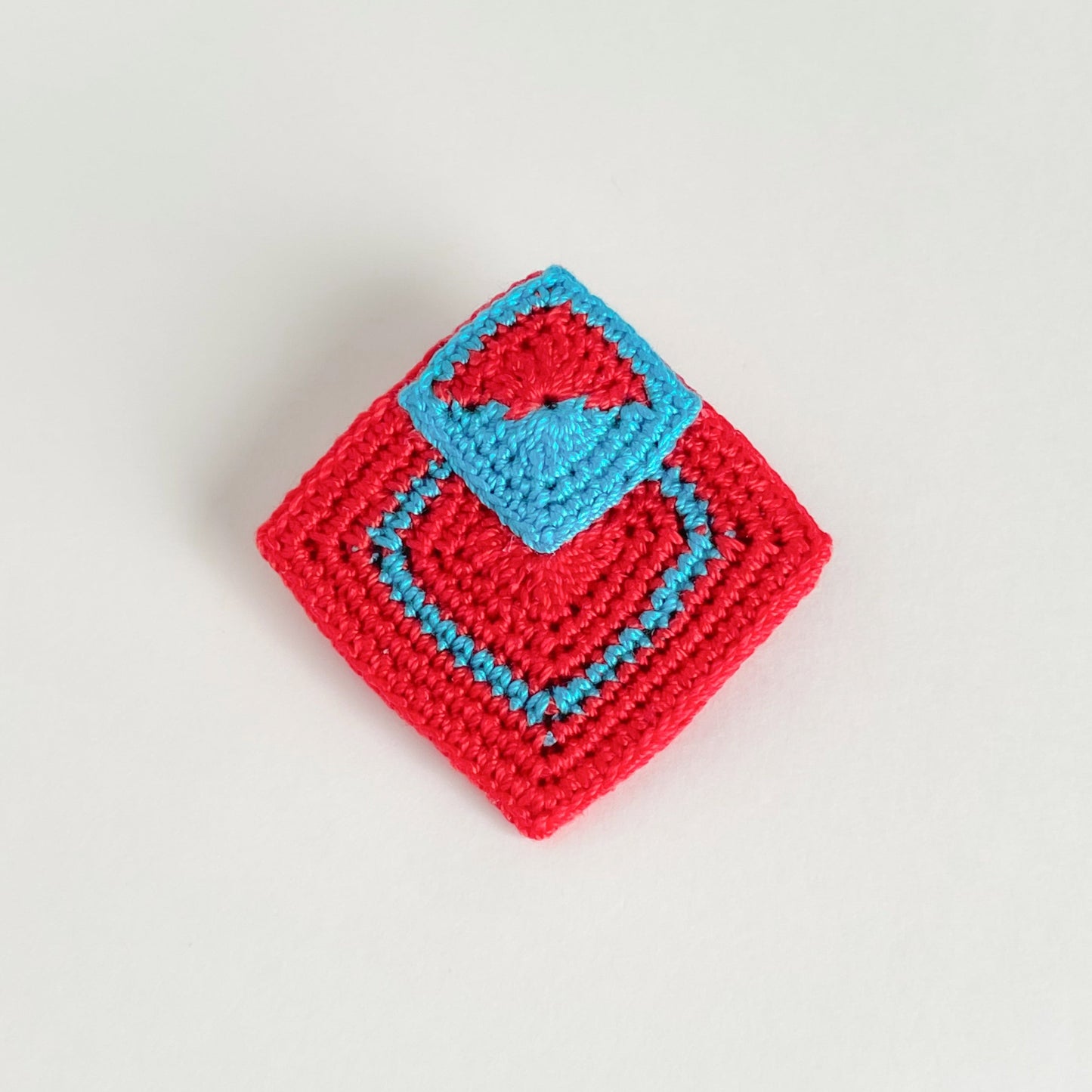 Handmade crochet geometric brooch in red and Caribbean blue (turquoise) with layered square motifs by Crochet by Heart.