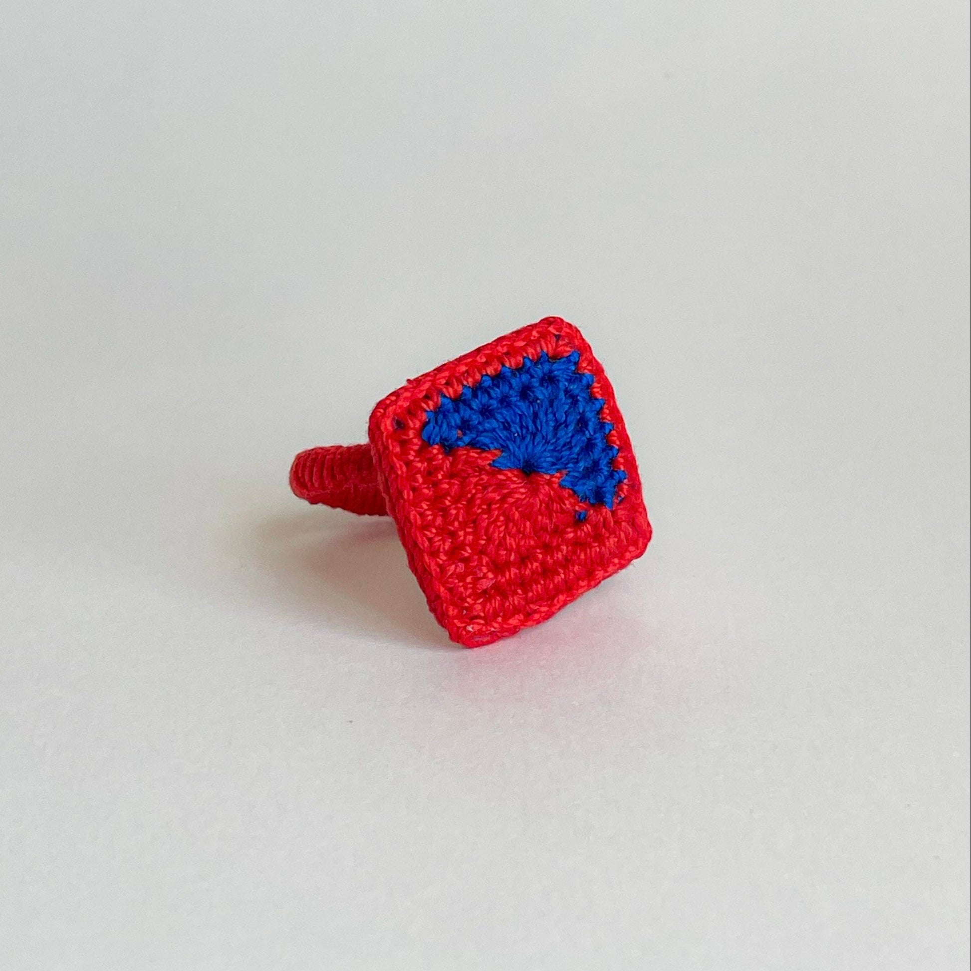 Red crocheted ring with a blue detail design on a light gray background