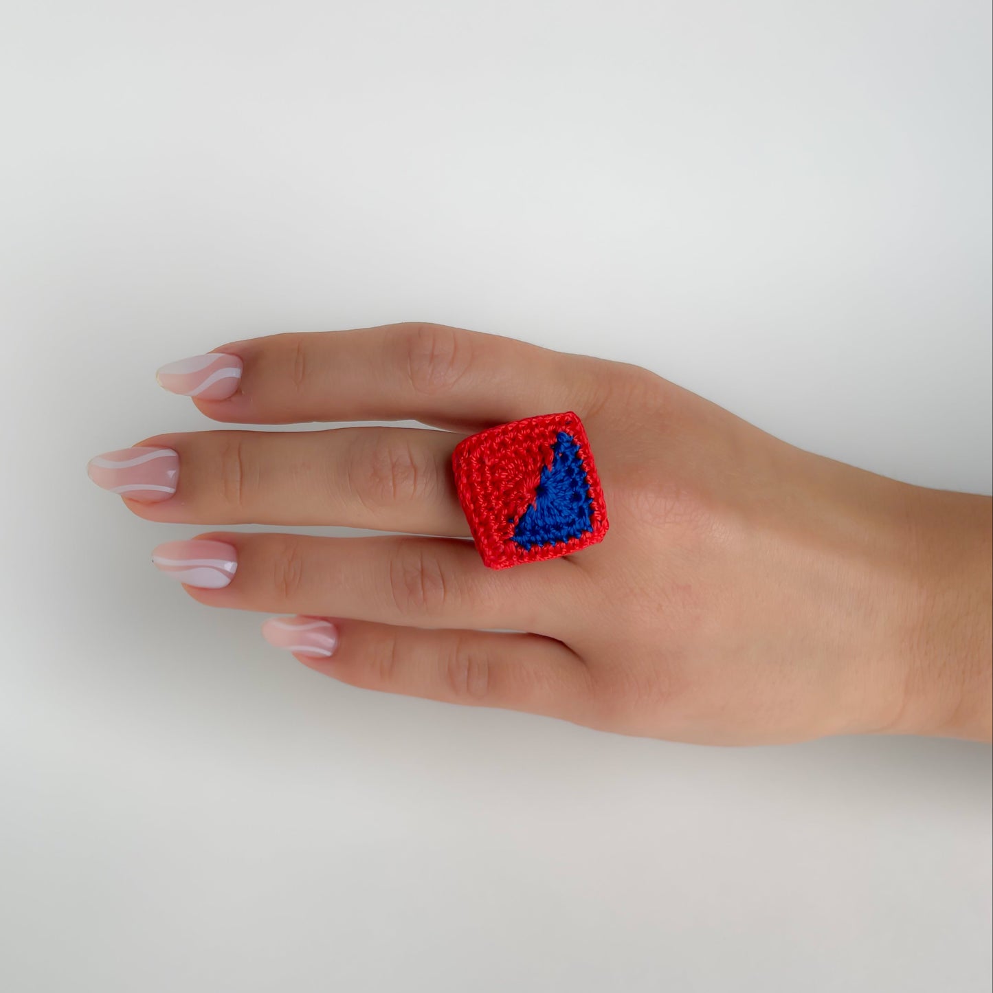 Hand wearing a red and blue Tessera crochet ring on a white background.