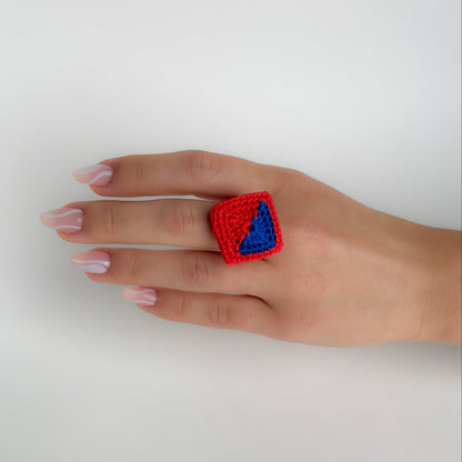 Hand wearing a red and blue Tessera crochet ring on a white background.
