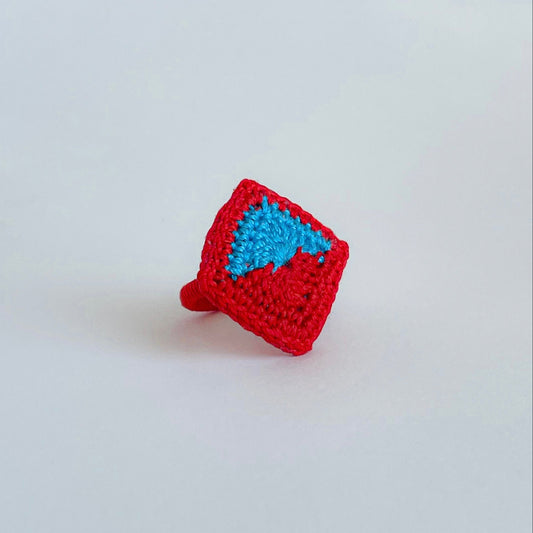 Crocheted ring with red diamond shape and Caribbean blue (turquoise) center on a light gray background