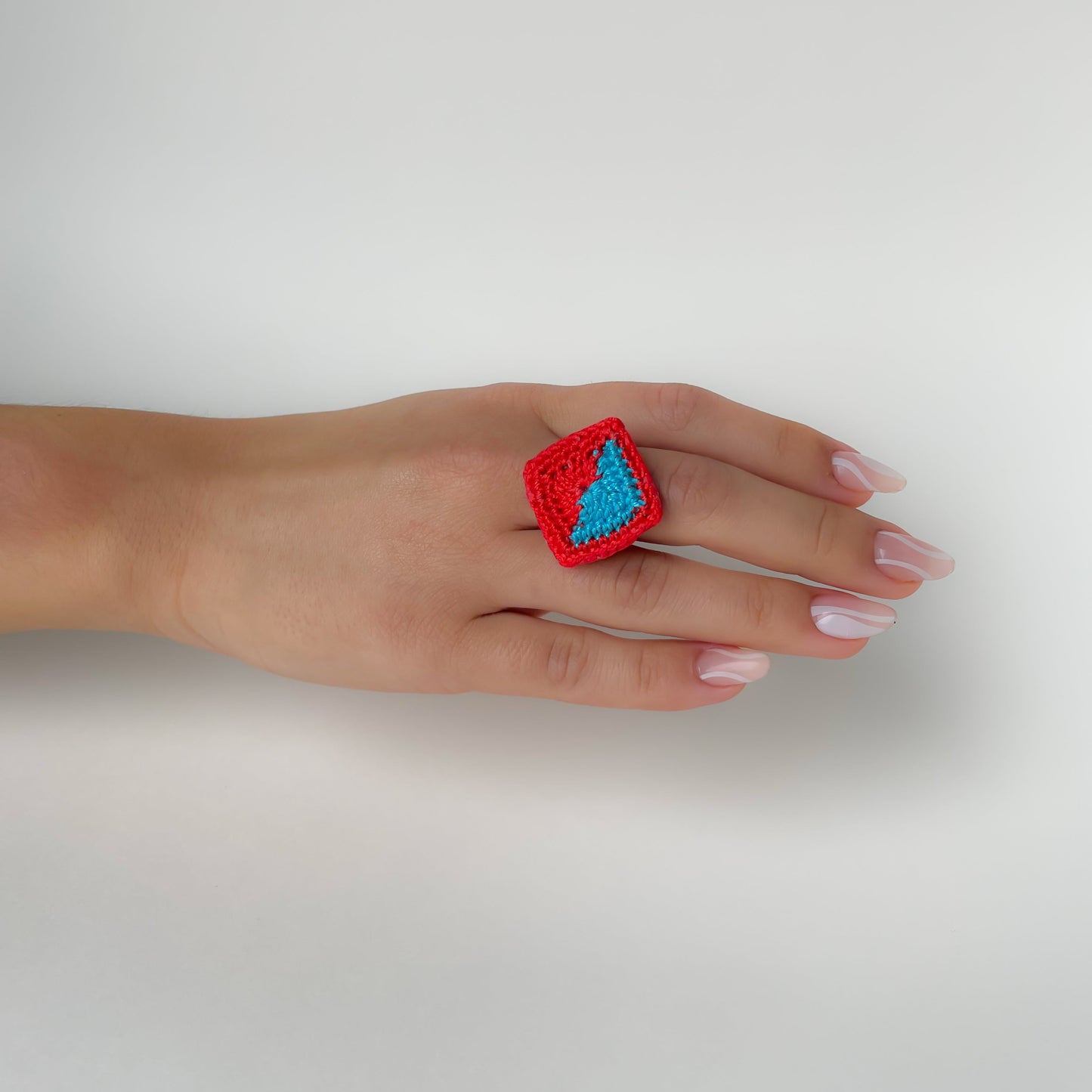 Hand wearing a red and Caribbean blue (turquoise) Tessera crochet ring on a white background.