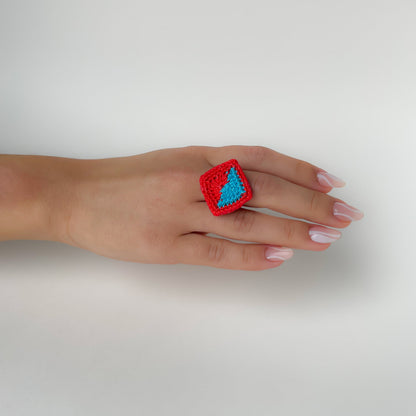 Hand wearing a red and Caribbean blue (turquoise) Tessera crochet ring on a white background.
