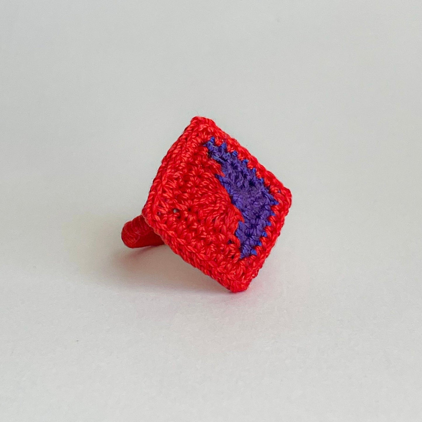Red crocheted ring with a violet detail design on a light gray background