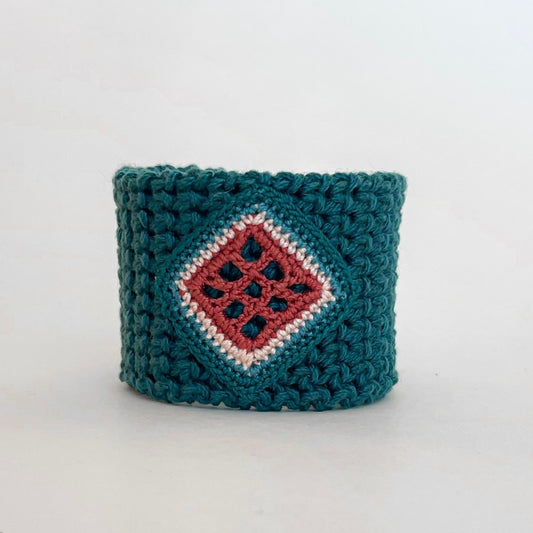 Front view of the TRAMA teal crochet cuff bracelet with a clay openwork motif bordered in ivory,  blue and teal.