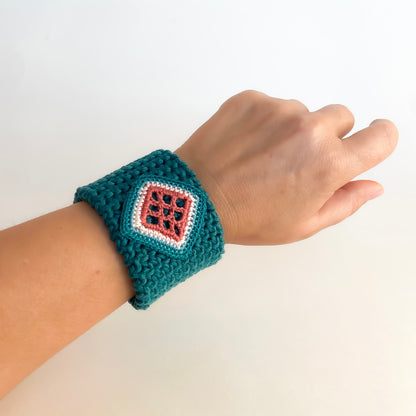 TRAMA teal crochet cuff bracelet with a clay and cream square motif, worn on the wrist.