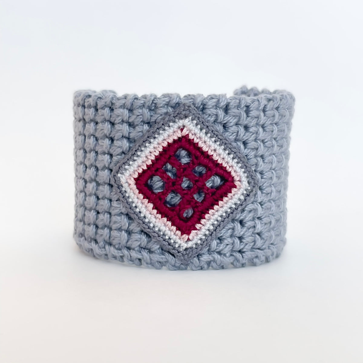 Front view of the TRAMA gray crochet cuff bracelet with a burgundy openwork motif bordered in rose, light gray and gray.