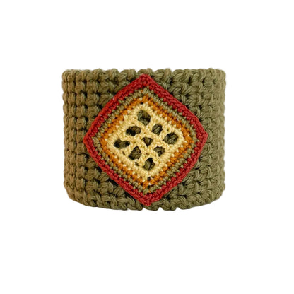 A handmade olive green crocheted cuff bracelet featuring a central diamond-shaped patch with yellow butter, ginger, moss green and cooper details, set against a plain light background.