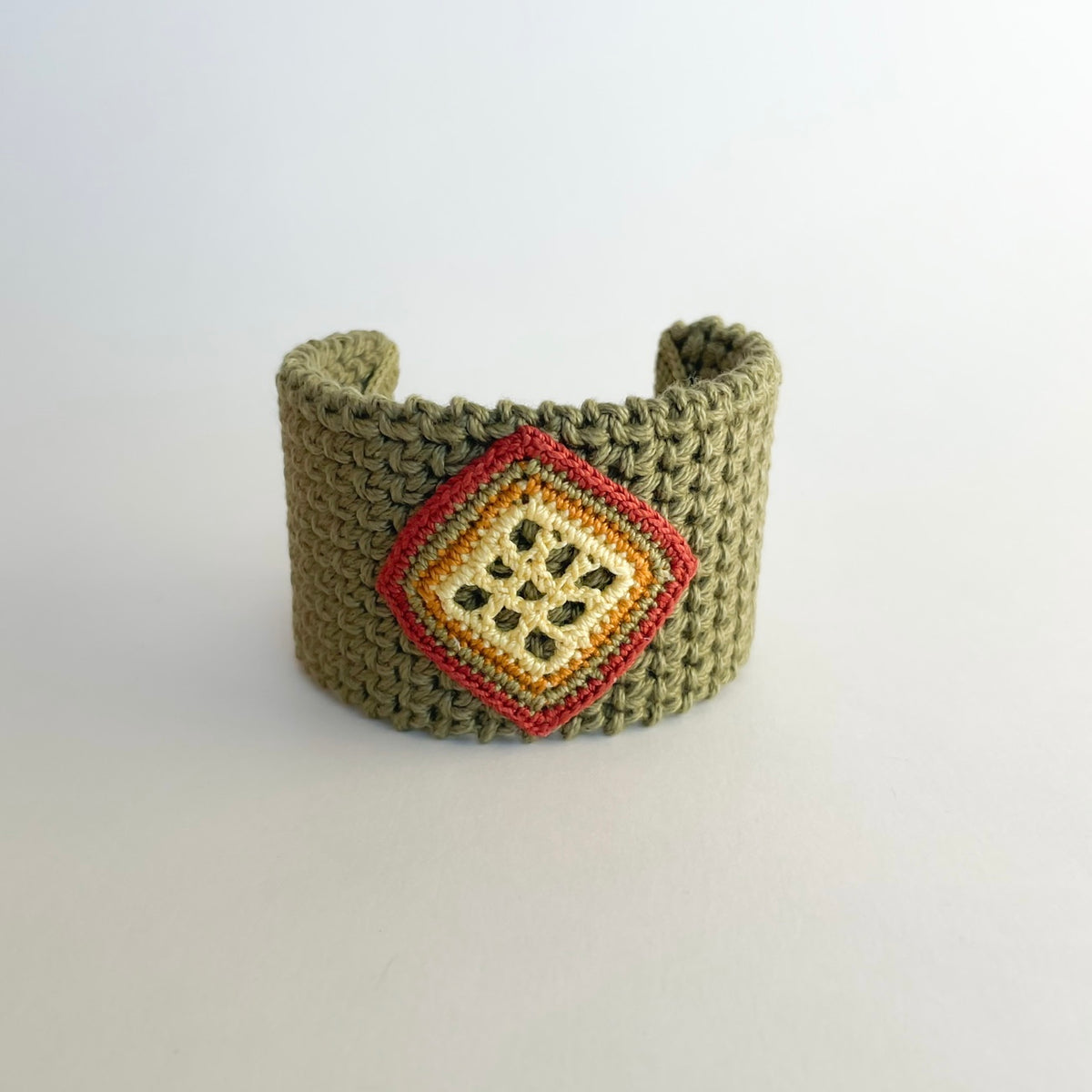 Front view of the TRAMA moss green crochet cuff bracelet with a pale yellow openwork motif bordered in yellow butter, ginger, green and cooper.