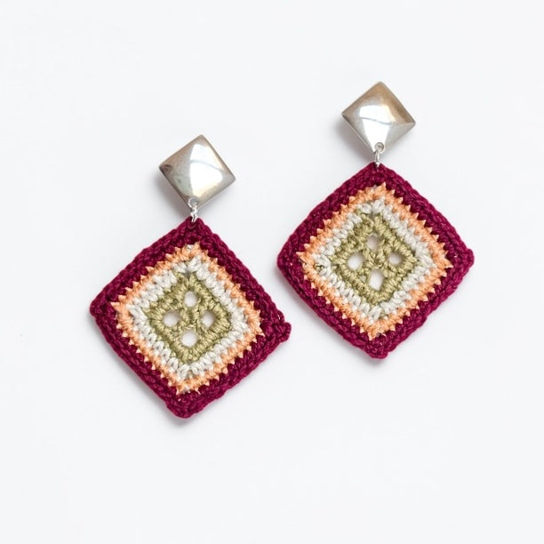 A pair of handmade square dangle earrings featuring a multi-colored crocheted pattern in burgundy, peach, cream, and olive green, suspended from faceted silver-toned cube studs.