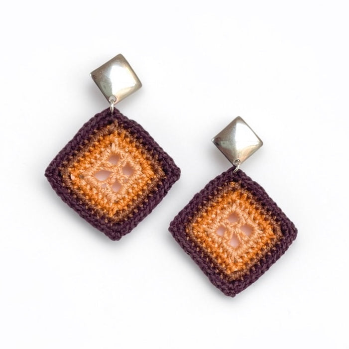 A pair of handmade crocheted dangle earrings featuring a square design with concentric bands of topaz, hemp, and chocolate, topped with metallic silver square studs, shown on a plain white background.
