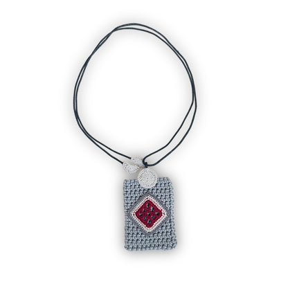 TRAMA crochet necklace with a gray rectangular pendant, an rose, cream and burgundy diamond motif, and a black cord on a white background.