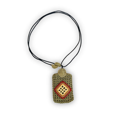 TRAMA crochet necklace with a moss green rectangular pendant, a yellow butter, ginger and clay diamond motif, and a black cord on a white background.