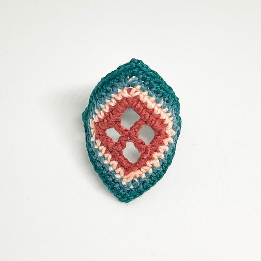 TRAMA teal crochet ring with an elongated diamond shape, clay openwork centre and pale cream border on a white background.