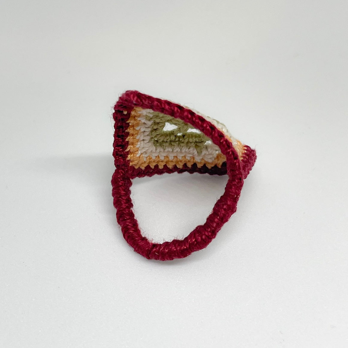 Back view of the TRAMA burgundy crochet ring with a moss green openwork motif bordered in ivory, marigold and burgundy.