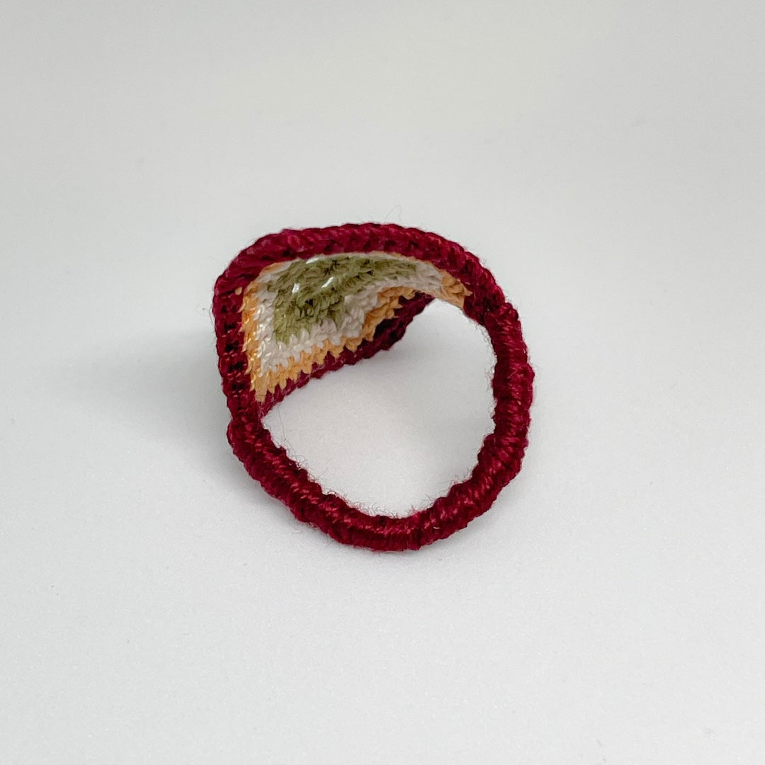 Back view of the TRAMA burgundy crochet ring with a moss green openwork motif bordered in ivory, marigold and burgundy.