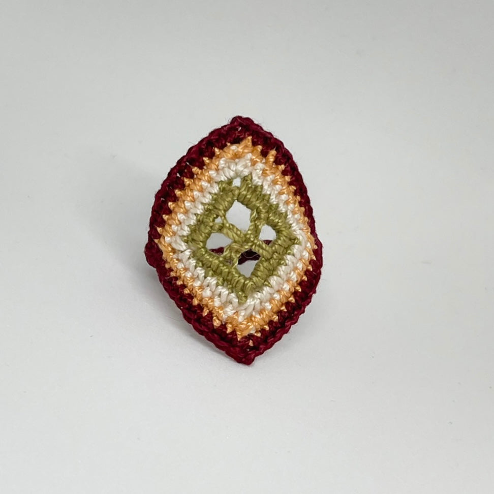TRAMA burgundy crochet ring with an elongated diamond shape, moss green openwork centre and marigold border on a white background.