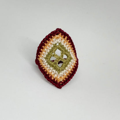 TRAMA burgundy crochet ring with an elongated diamond shape, moss green openwork centre and marigold border on a white background.