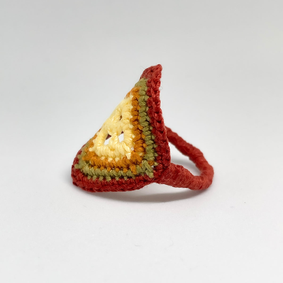 Side view of the TRAMA crochet ring with a yellow butter centre, ginger, moss green and copper borders, showing the cooper crochet band.