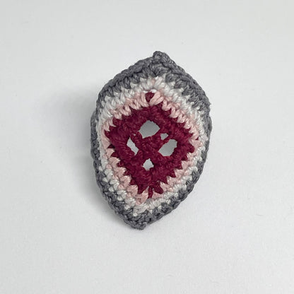 TRAMA gray crochet ring with an elongated diamond shape, burgundy openwork centre and rose border on a white background.
